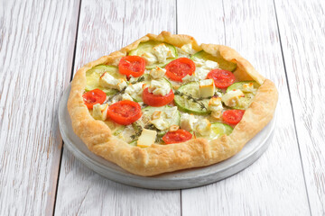 Rustic homemade galette with cheese and vegetables on a light rustic background.