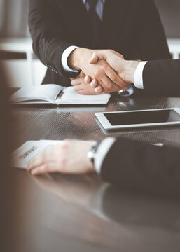Unknown businessmen shaking hands above the glass desk in a modern office, close-up. Unknown business people at meeting. Teamwork, partnership and handshake concept