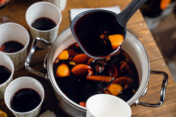 Red mulled hot and spiced wine alcohol drink pouring into disposabla glass. Grog with cinnamon...