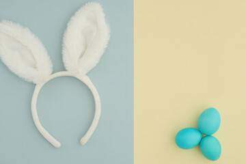 A minimalistic two-tone background in pastel shades cut in half. Easter background with bunny white ears on a blue background and three blue Easter eggs on a yellow background. Space for text