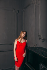 Fototapeta na wymiar beautiful girl in a red dress stands against a dark wall