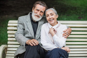 Elegant mature man and woman resting at green park, smiling and hugging. Happy aged couple sitting...