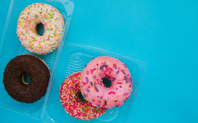 Sweet donuts of different colors in a plastic container on a blue background. Confectionery products.