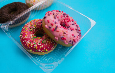 Sweet donuts of different colors in a plastic container on a blue background. Confectionery...