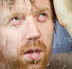 Whte man under shower water streams, dynamic face with beard