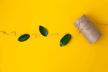 Creative composition with natural jute twine roll and green leaves, on yellow background with copyspace for text or your presentation. Handmade and ecological packaging concept, sustainable lifestyle.