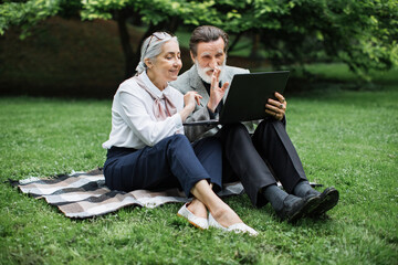Fototapeta premium Beautiful mature couple in elegant clothes talking and waving during video call on wireless laptop. Concept of people, technology and retirement.