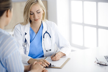 Woman-doctor and patient sitting and talking in hospital or clinic. Blonde therapist is cheerfully smiling. Medicine concept