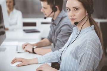 Fototapeta premium Call center. Group of casual dressed operators at work. Brunette business woman in headset at customer service office