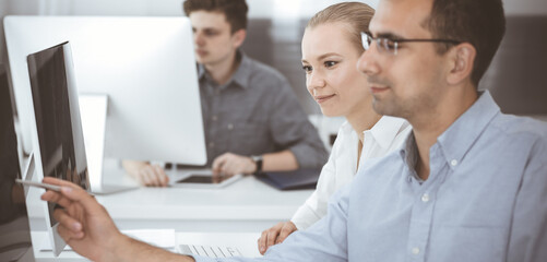 Fototapeta premium Business people working together in modern office. Happy smiling adult businessman using pc computer with colleagues. Teamwork and partnership concept