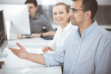 Obraz premium Business people working together in modern office. Happy smiling adult businessman using pc computer with colleagues. Teamwork and partnership concept