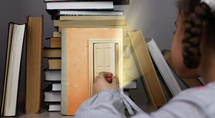 Smart cute girl opening a tiny door in the house of books, beam of lights through the door, studio shot, study and education concept
