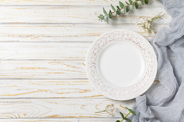 Festive table setting with empty white plate with ornament, gray napkin and eucalyptus leaves on...
