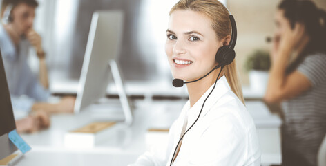 Blonde business woman using headset for communication and consulting people at customer service office. Call center. Group of operators at work