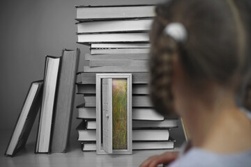 Smart cute girl opening a tiny door in the house of books, beam of lights through the door, studio shot, study and education concept