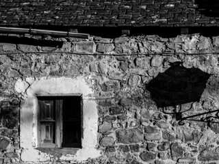 Una fachada de piedra con una ventana enmarcada con moldura encalada y la sombra de una farola en una imagen en blanco y negro de una aldea de montaña del Pirineo español