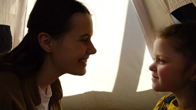 Close up of happy young mother and little child daughter playing bonding touching noses laughing together sitting in comfy tent, affectionate charming mom having fun with cute small kid enjoy cuddling