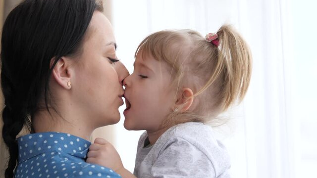 A little girl kisses her beloved mother, mom holds the child in her arms and hugs, the concept of a happy family life, the nanny calms the child, the parent is next to the kid together, 4K, close-up