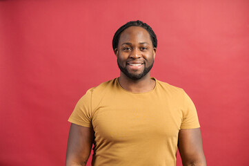 Friendly and positive African-American with dreadlocks guy wearing bright t-shirt looks at camera...