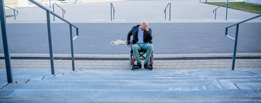 Image of depressed disabled man sitting in the wheelchair and facing the difficulties with climbing the stairs alone. Many stairs.