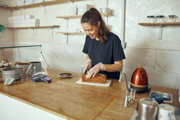 Female barista at showcase with desserts in cafe. Young worker of sweet shop and cafe