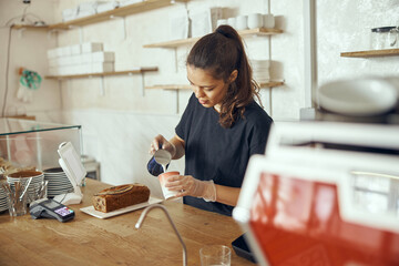 Young female woman barista pouring fresh milk to prepare latte coffee for customer in cafe. For small business startup in food industry concept