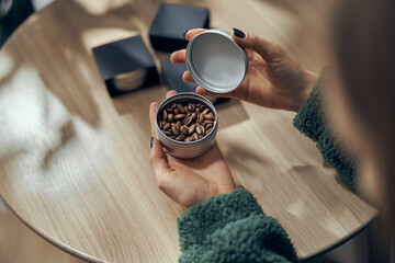 Female hand holds bowl of ground coffee and beans in gift box on the table
