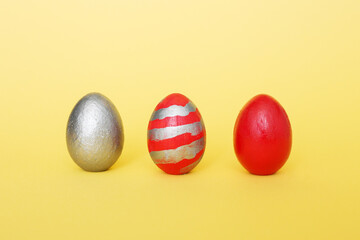 abstract composition of three multi-colored handmade eggs on a yellow pastel background. Eggs of metallic, red, red with gray stripes on a yellow paper background.