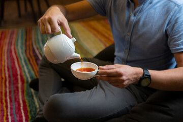 Man pouring tea into white cup