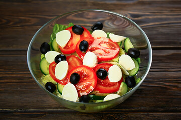 Vegetable salad on a wooden background. Lettuce, tomato, cucumber, olives, mozzarella and olive oil. Wholesome healthy food.