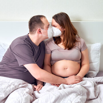 A man and a pregnant woman kiss in medical masks n95 ffp2. Coronavirus problems and excessive protection
