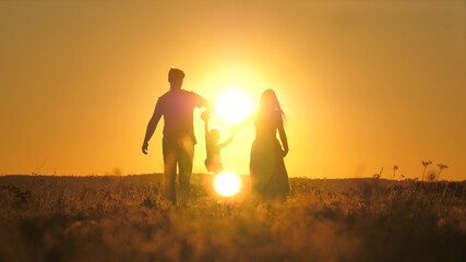 A small child walks with mom and dad at a bright sunset in the sky. Meet the sunrise with your family while traveling. Go hiking with your mother and father. Kid and loving parents walk in the park