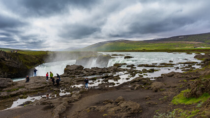several tourists taking photos and selfies near the Godafoss waterfall in Iceland during summer season