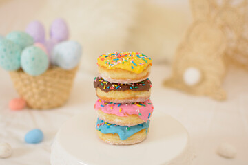Tower of stacked sweet and colorful donuts with sprinkled chocolate icing and small Easter eggs in the background