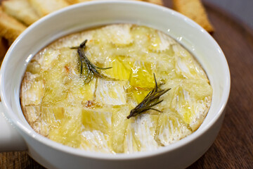 A plate of hot baked camembert cheese with rosemary close-up.