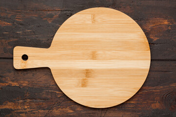 Round wooden cutting board for pizza ondark wooden background. Top view. Mock up for food project.