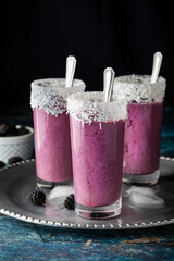 Three berry smoothies garnished with coconut shavings on a metal tray ready for drinking.