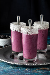 Three berry smoothies with tall spoons on a metal tray, garnished with coconut shavings against a black background.
