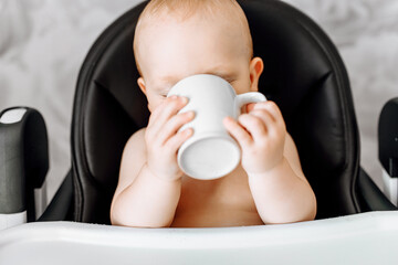 baby drinking water from a mug sitting in a baby feeding chair