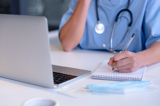 Midsection of caucasian female doctor using laptop taking notes during video call consultation