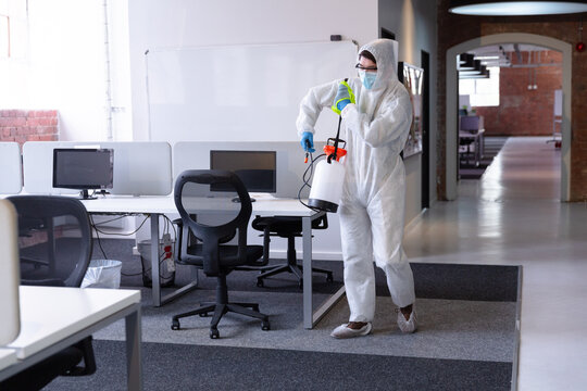 Cleaner wearing hygiene overalls, gloves and face mask carrying disinfectant in office