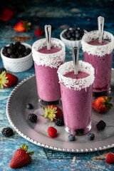 Close up of three berry smoothies on a metal tray surrounded by several berries.