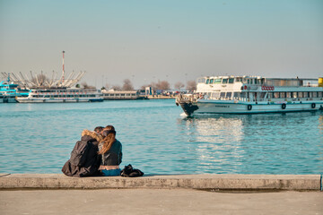 Turkey istanbul 04.03.2021. Two young couples and lovers hugging each other and sitting against bosporus in Kadikoy istanbul during sunny day with passenger ferry and turquoise water background.