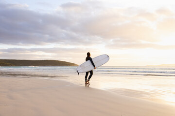 young woman heading into the surf carrying long board