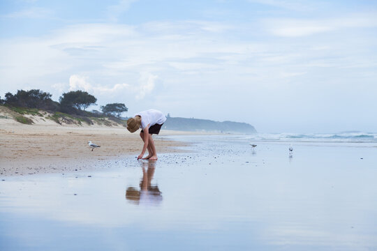 Young woman walking along beachcombing looking for shells at the seaside