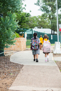 Young school kids walking along footpath with bags on