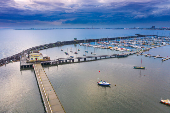 Aerial view of a long narrow jetty over a calm bay under a dark twilight sky