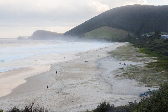 People walking along blueys beach at sunset