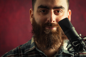 Young hipster man near a streaming microphone smiling with a red background and copy space