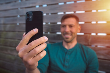Young happy man with smartphone outdoors at sunset. Man using modern black smartphone. Man having a facetime video call. Looking at smartphone 